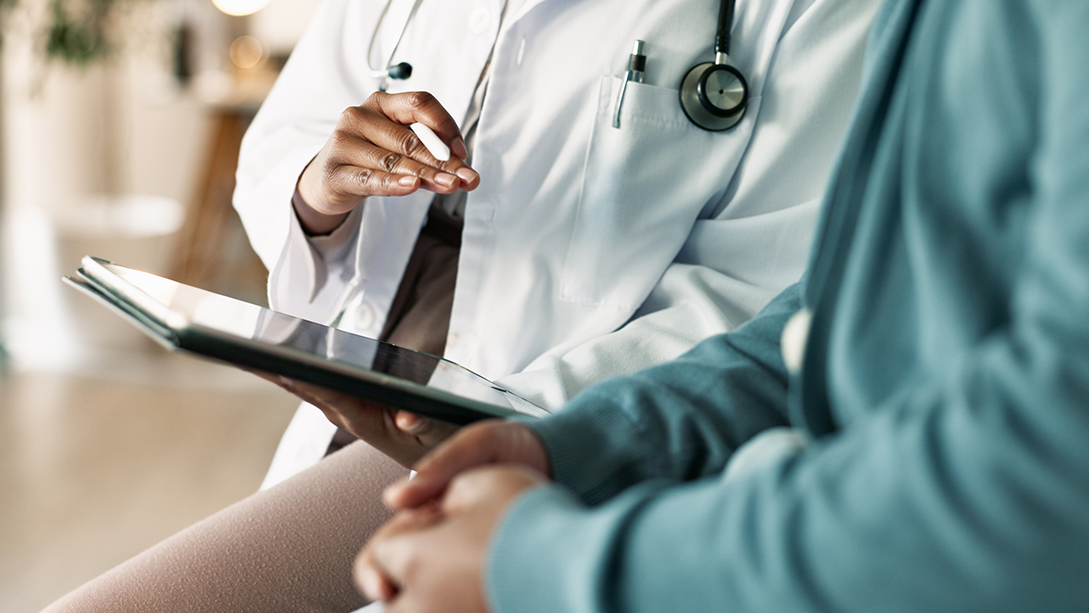 Un gros plan d’un médecin, une tablette à la main, assis à côté d’un patient.